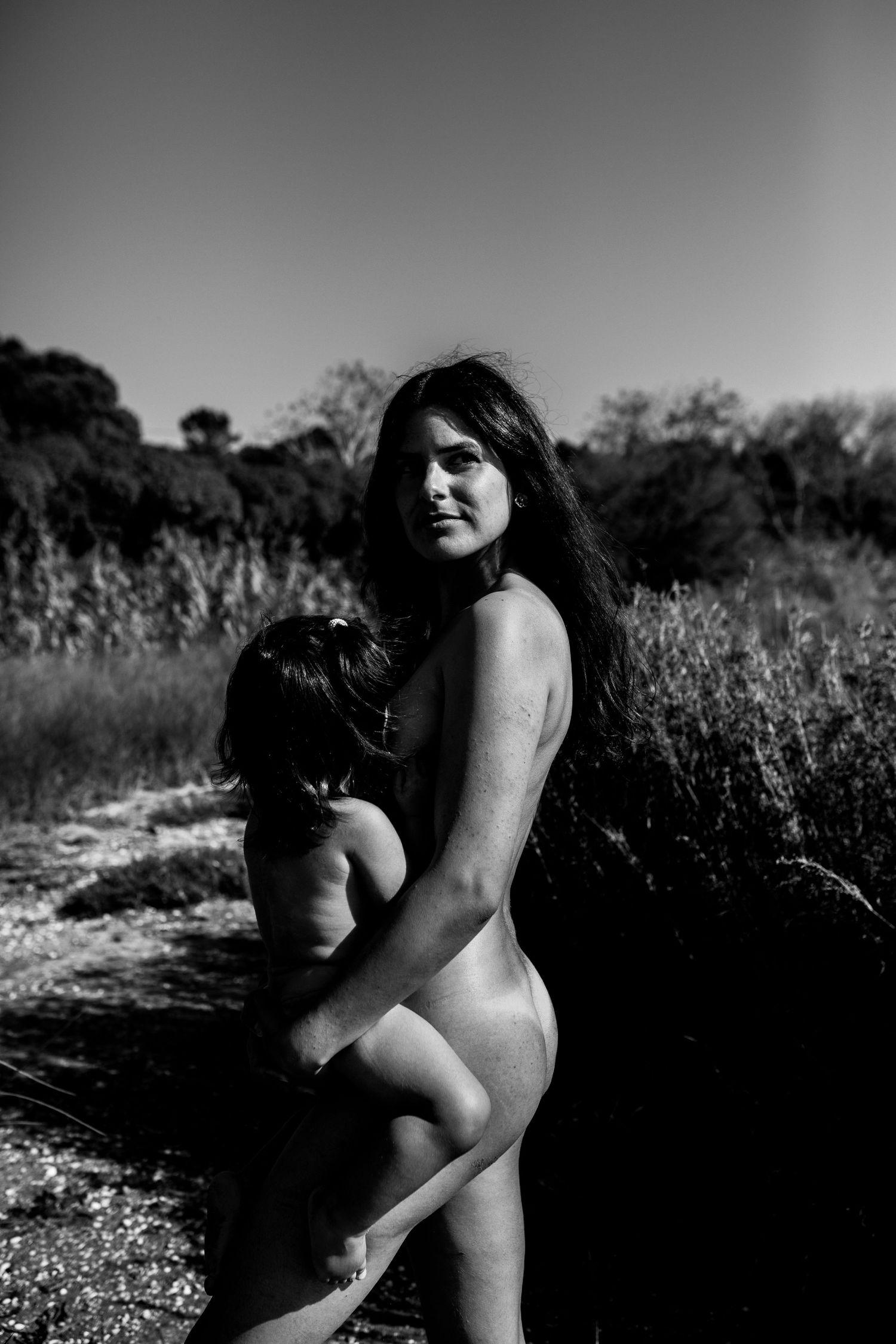 Black and white artistic nude photograph showing silhouette against natural outdoor background.