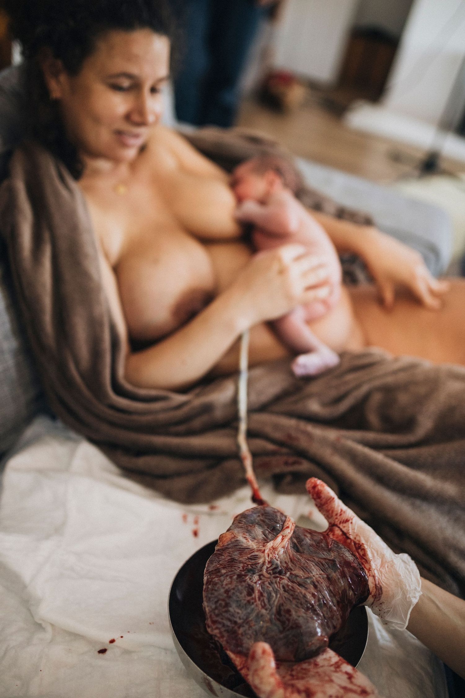 Medical professional examining placenta after birth while mother bonds with newborn.