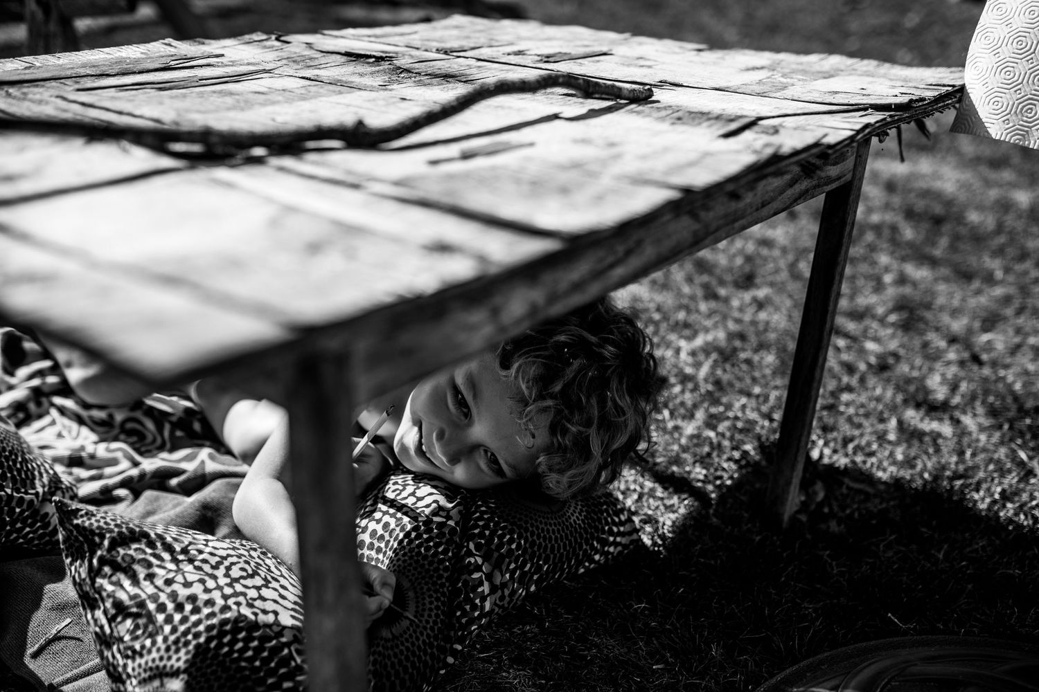 Person resting under wooden shelter in black and white countryside scene.