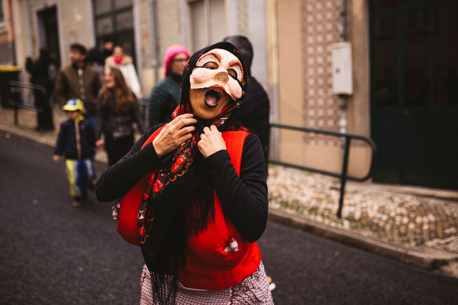 A person in a red sweater takes photos with a camera while standing on a cobblestone street.