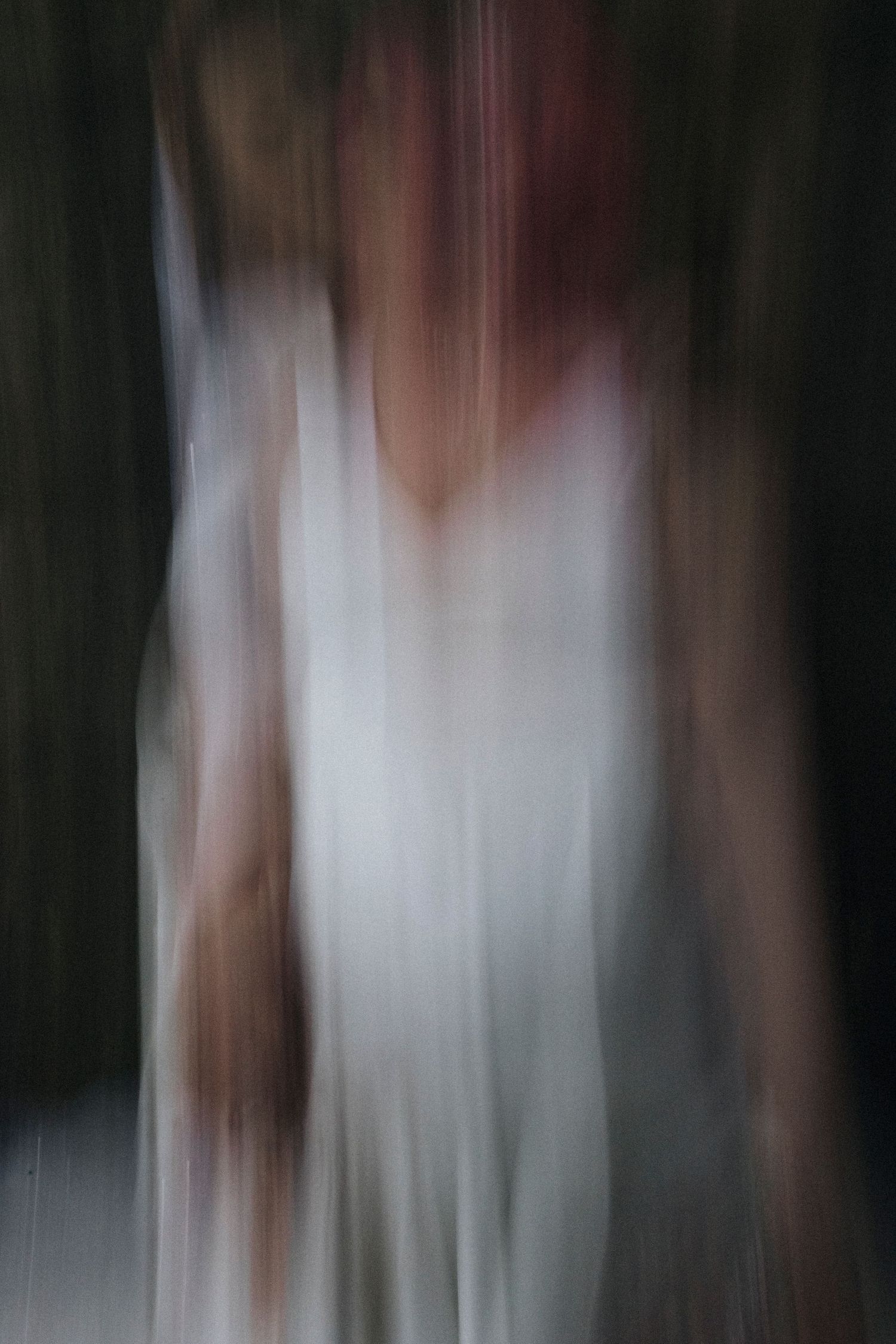 Abstract motion-blurred photograph creates dreamy effect with white dress and dark background.