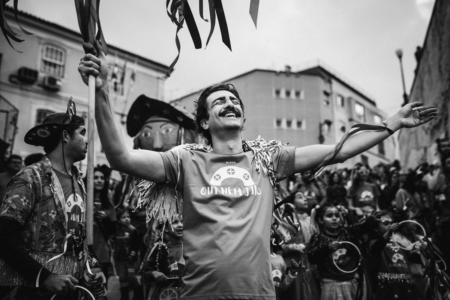 Black and white photo of people dancing and celebrating in the streets during a festival or carnival.