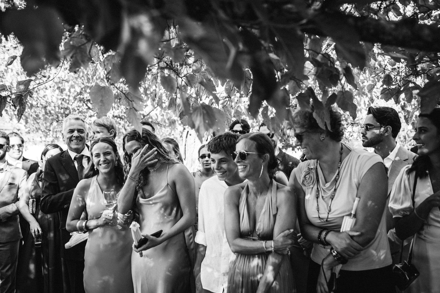 Black and white image of wedding guests enjoying an outdoor celebration.