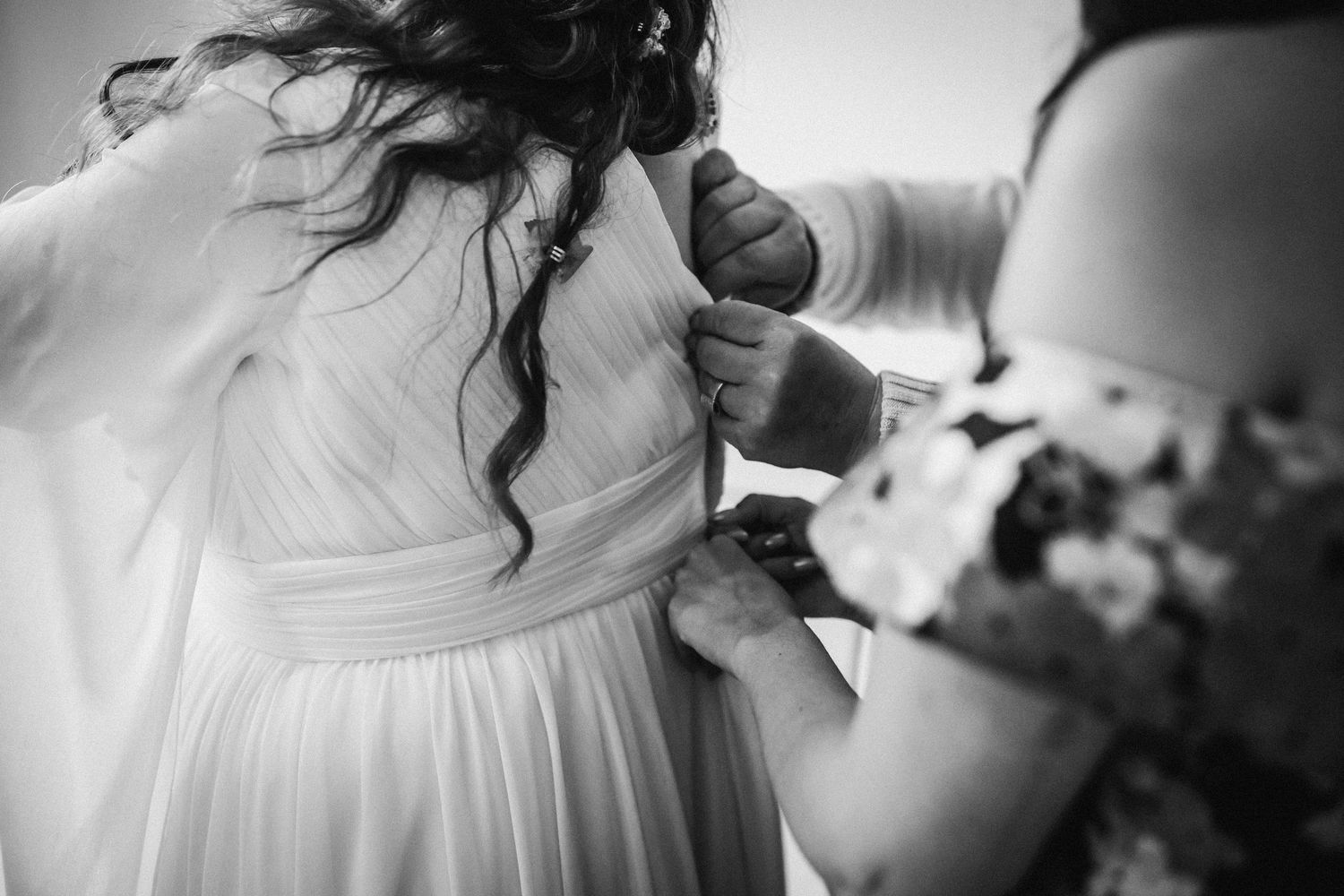 Close-up black and white photo of white wedding dress being fastened.