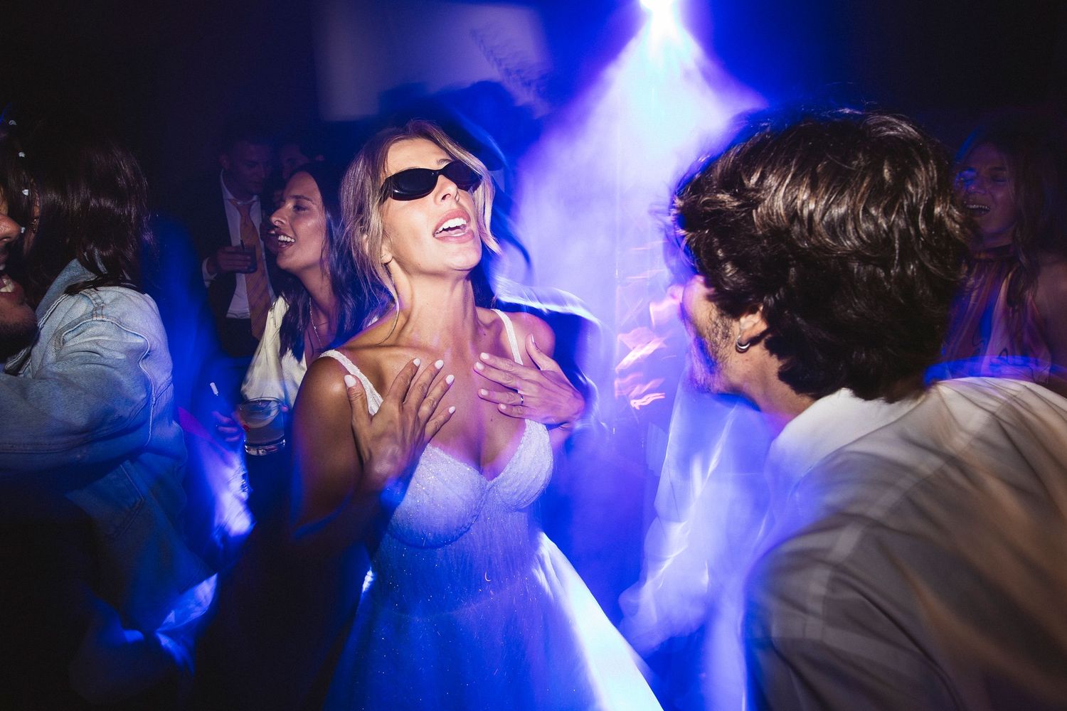 People dancing and celebrating at a wedding reception with dramatic blue lighting effects.