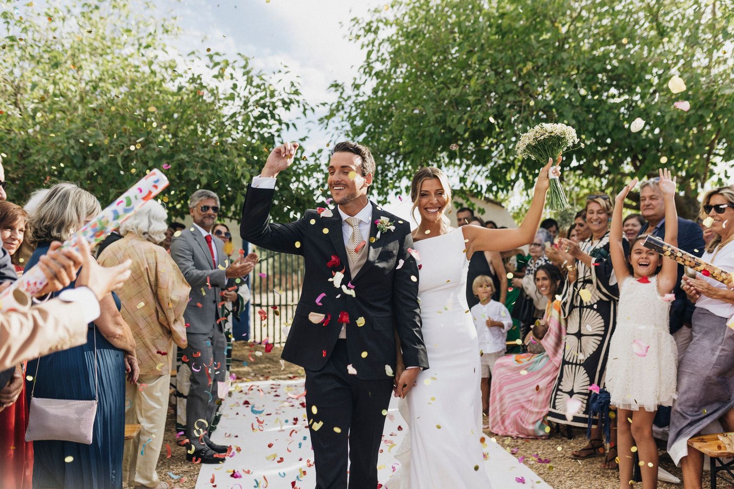 Wedding guests throw flower petals during an outdoor celebration.
