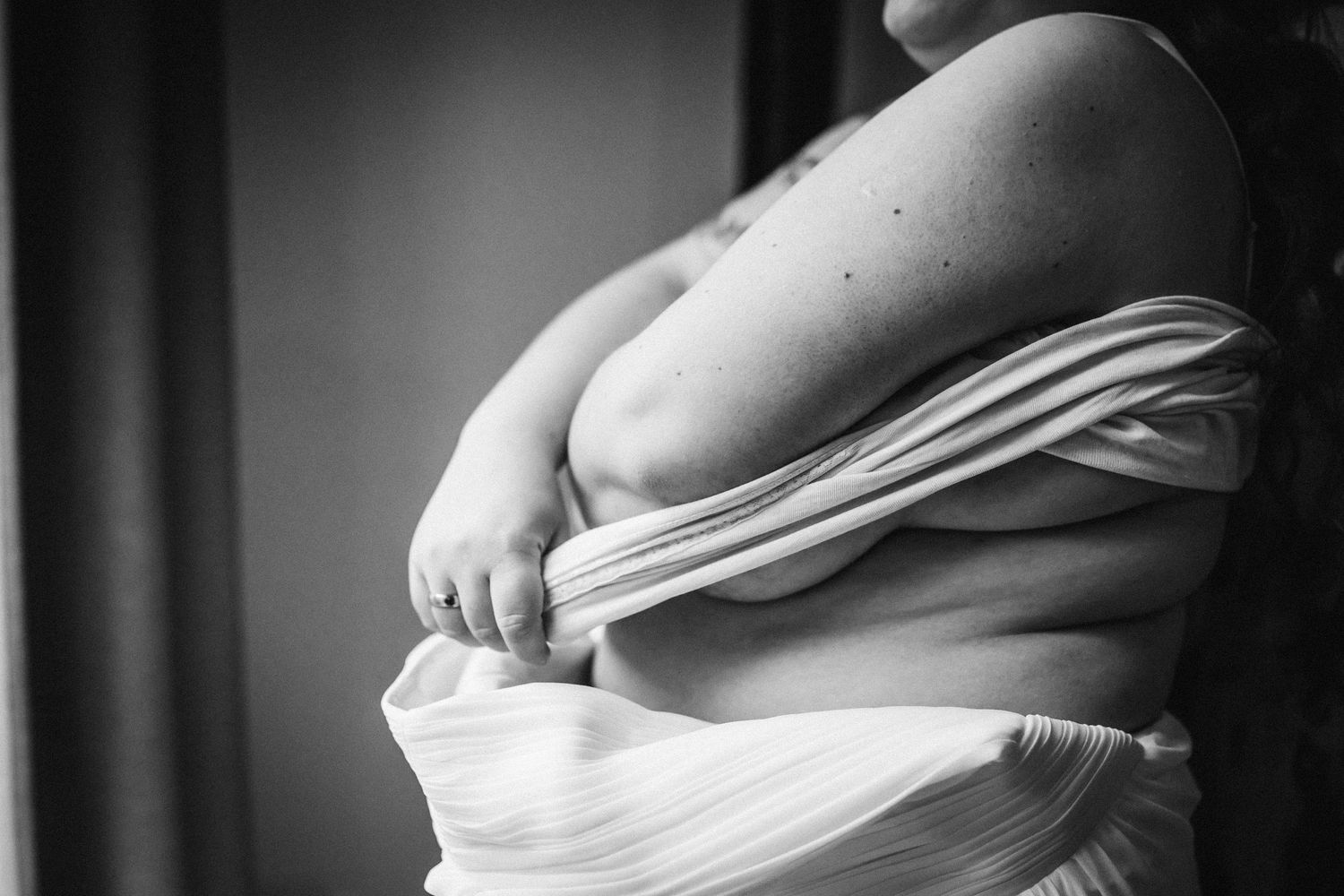 Artistic black and white maternity photo showing pregnant belly draped in flowing white fabric.