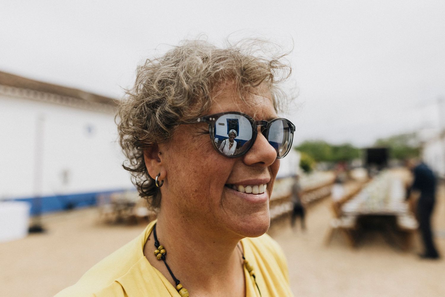 A person wearing sunglasses and a yellow shirt smiles while enjoying time outdoors on a sunny day.