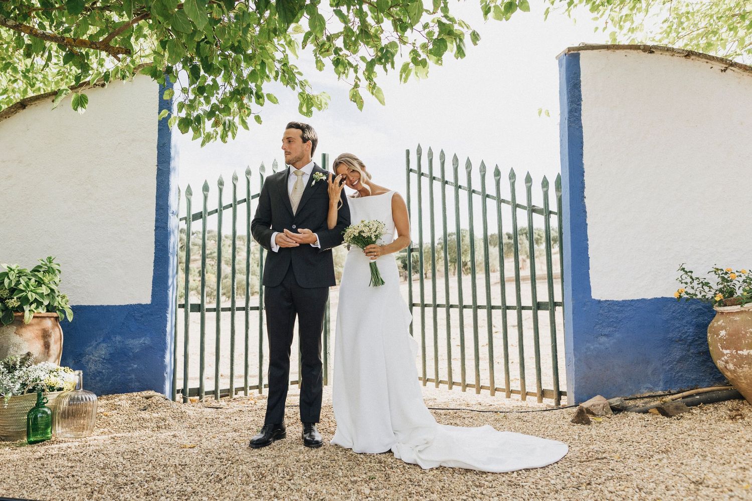 Outdoor wedding scene with white walls and blue trim featuring guests on a gravel path.