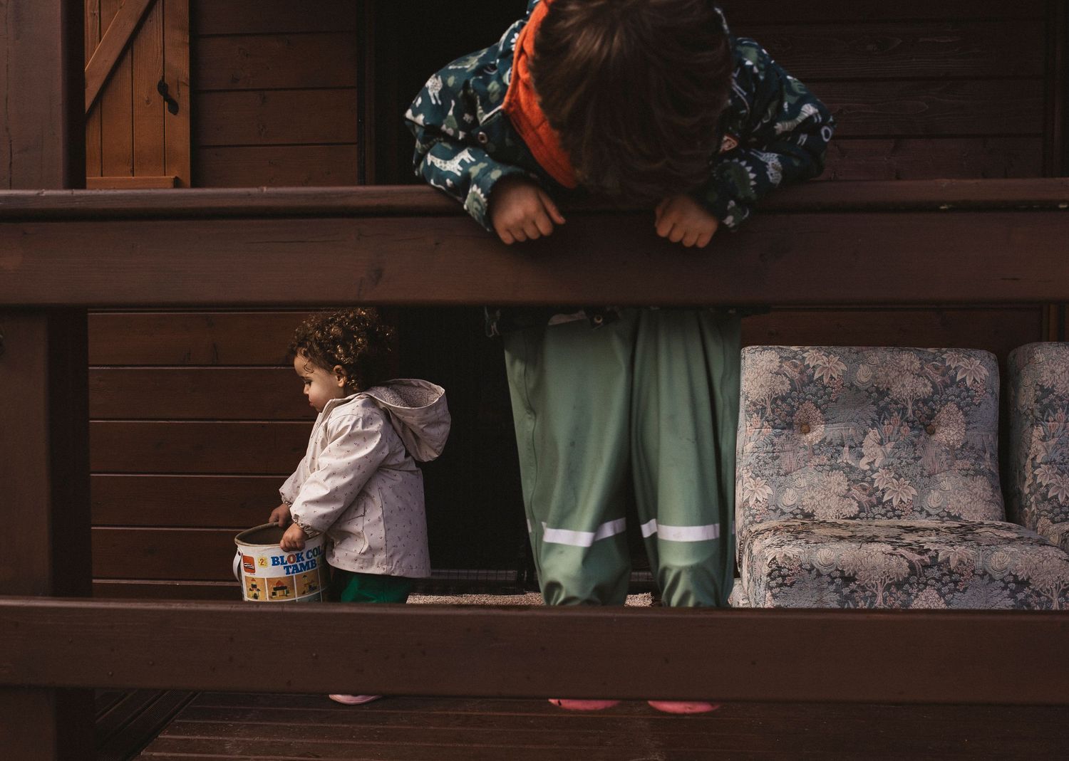 Feet in white shoes and pale clothing sitting on dark wooden steps in a dimly lit setting.