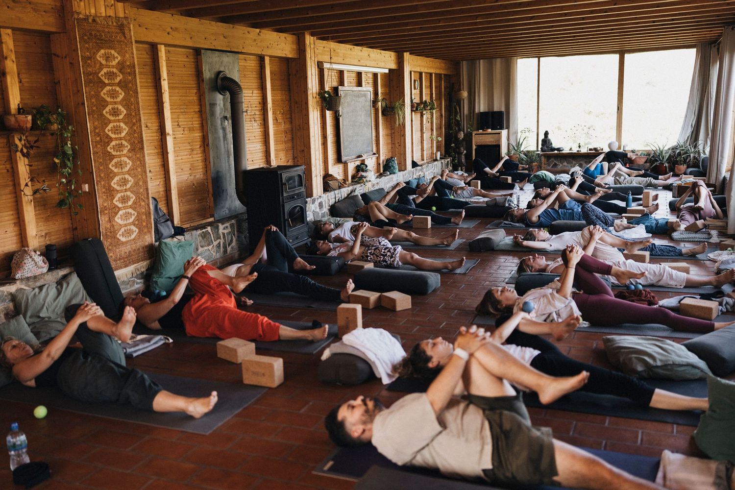 Students lying down in relaxation pose during a yoga class in a wooden studio.