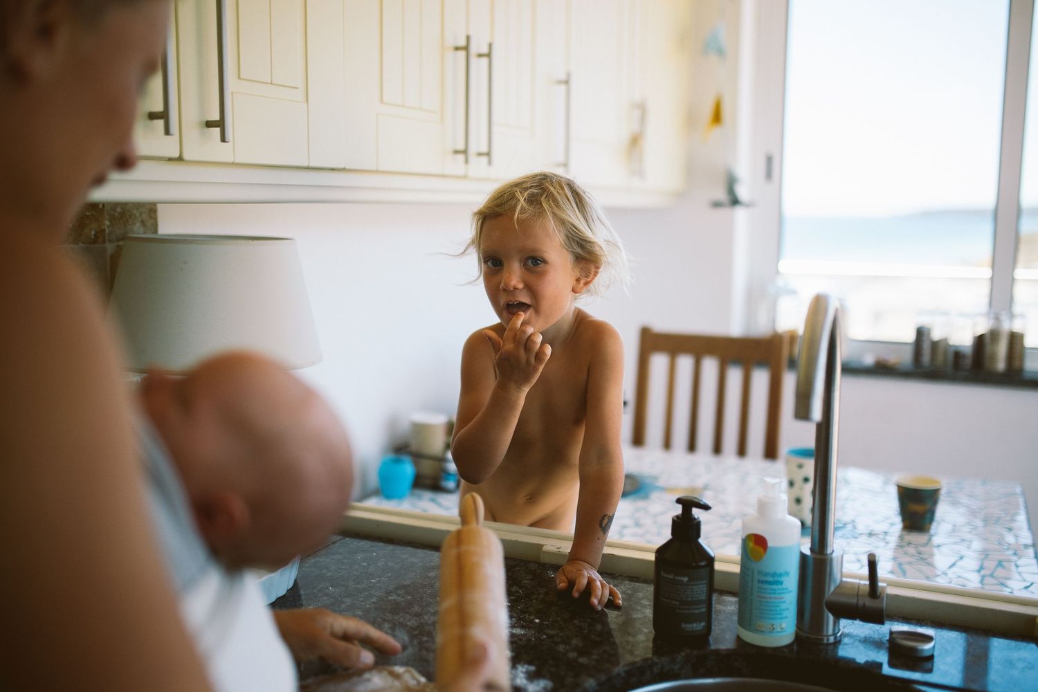 A person in a kitchen reaches for items in a white cabinet while preparing food.