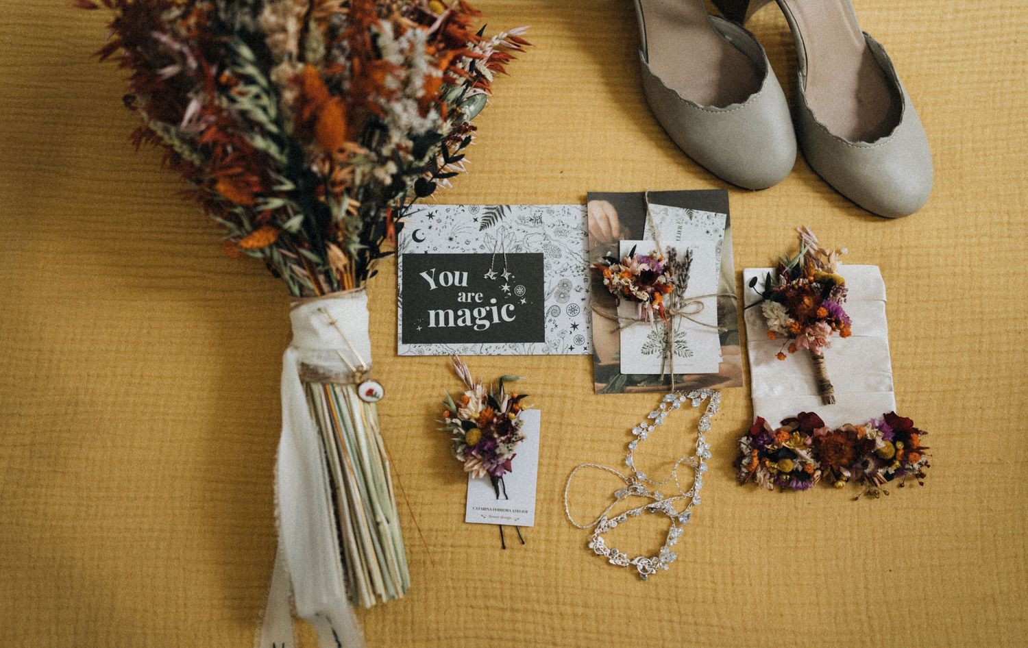 Elegant wedding accessories including shoes, floral wreath, and decorative elements arranged on beige background.