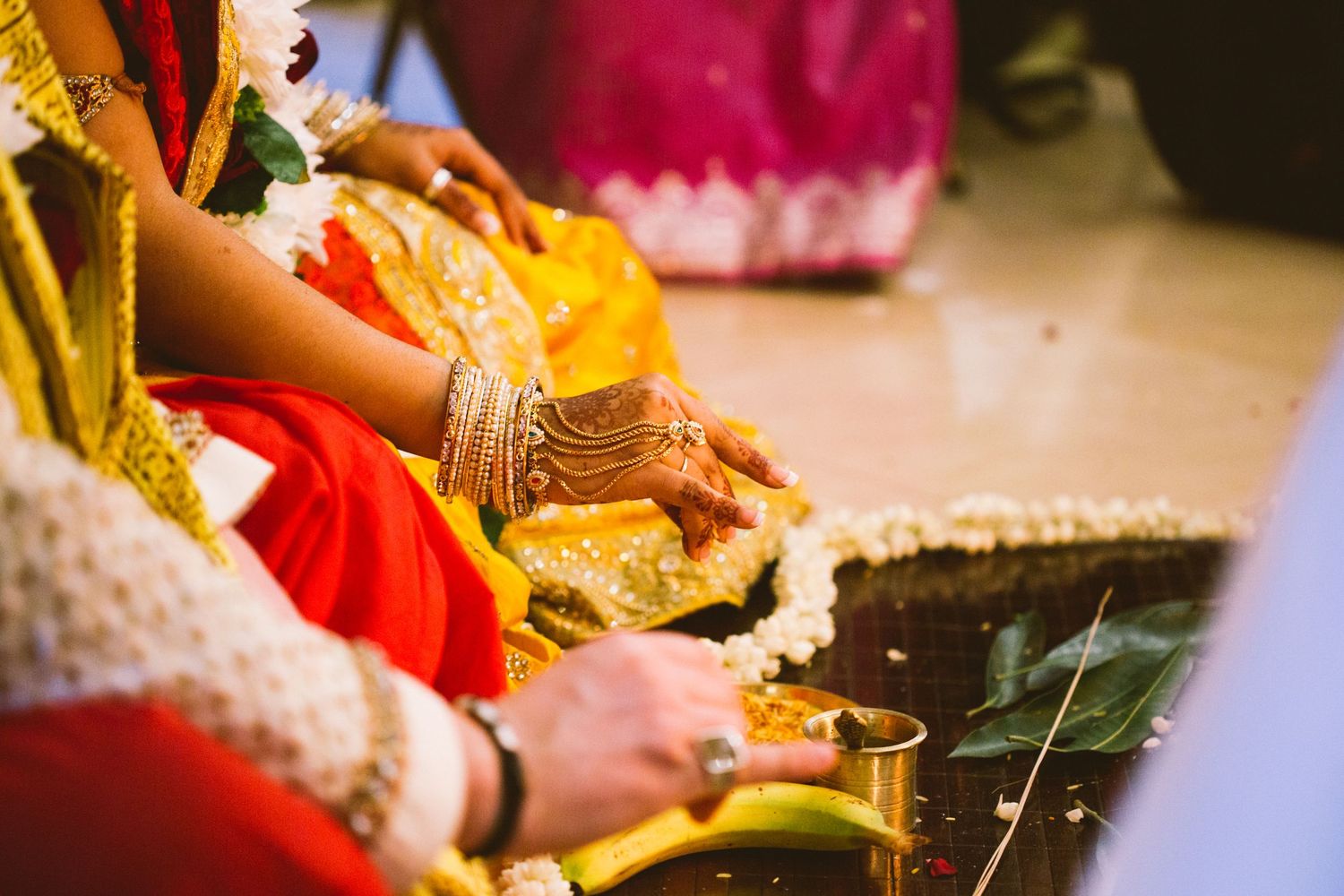 Traditional Indian wedding ceremony with hands performing rituals and decorative elements in warm lighting.