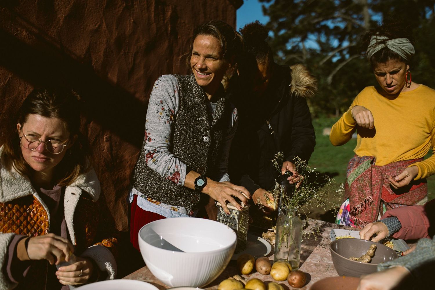 Friends gather outdoors for a casual meal with bowls and fresh fruit on the table.