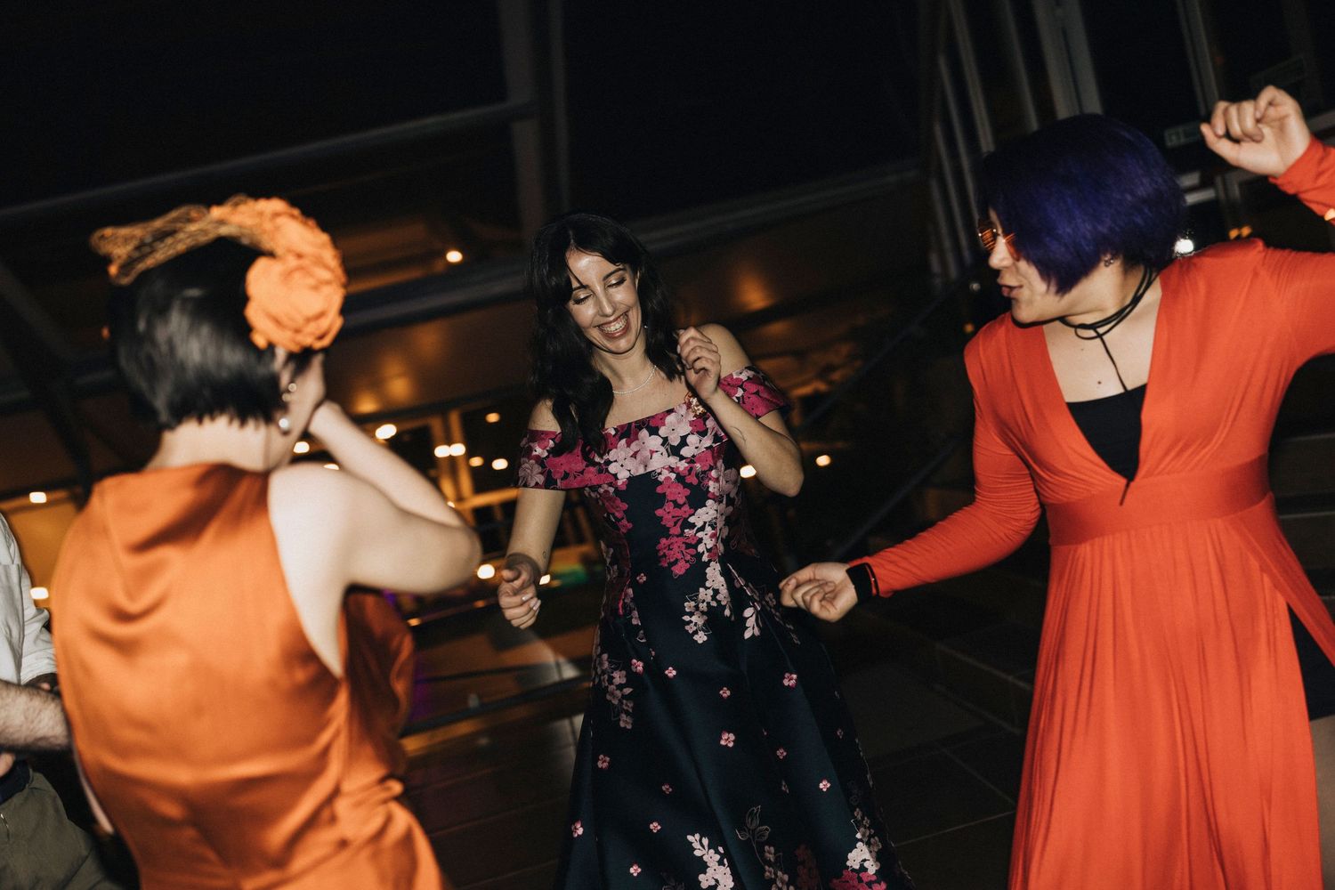 Wedding guests in orange and navy dresses dance together on a dimly lit dance floor during a celebration.