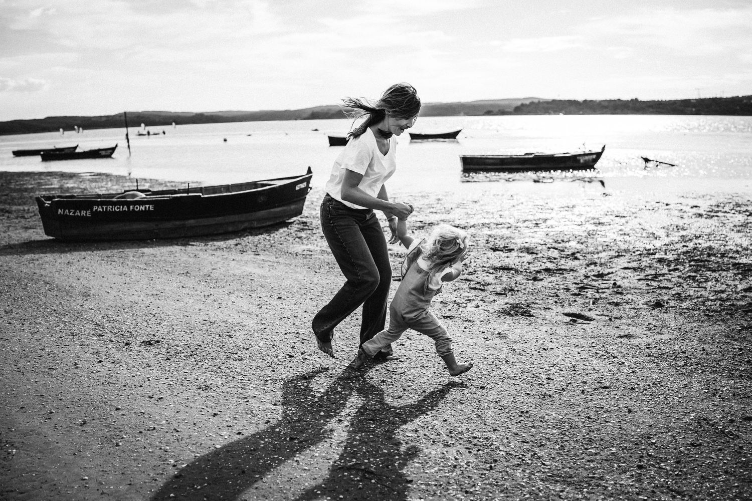 Black and white images capture joyful movement along a beach shore with boats in the background.
