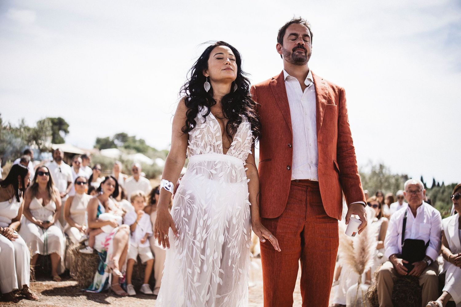 Wedding celebration outdoors with guests in white attire surrounding a couple in formal dress.