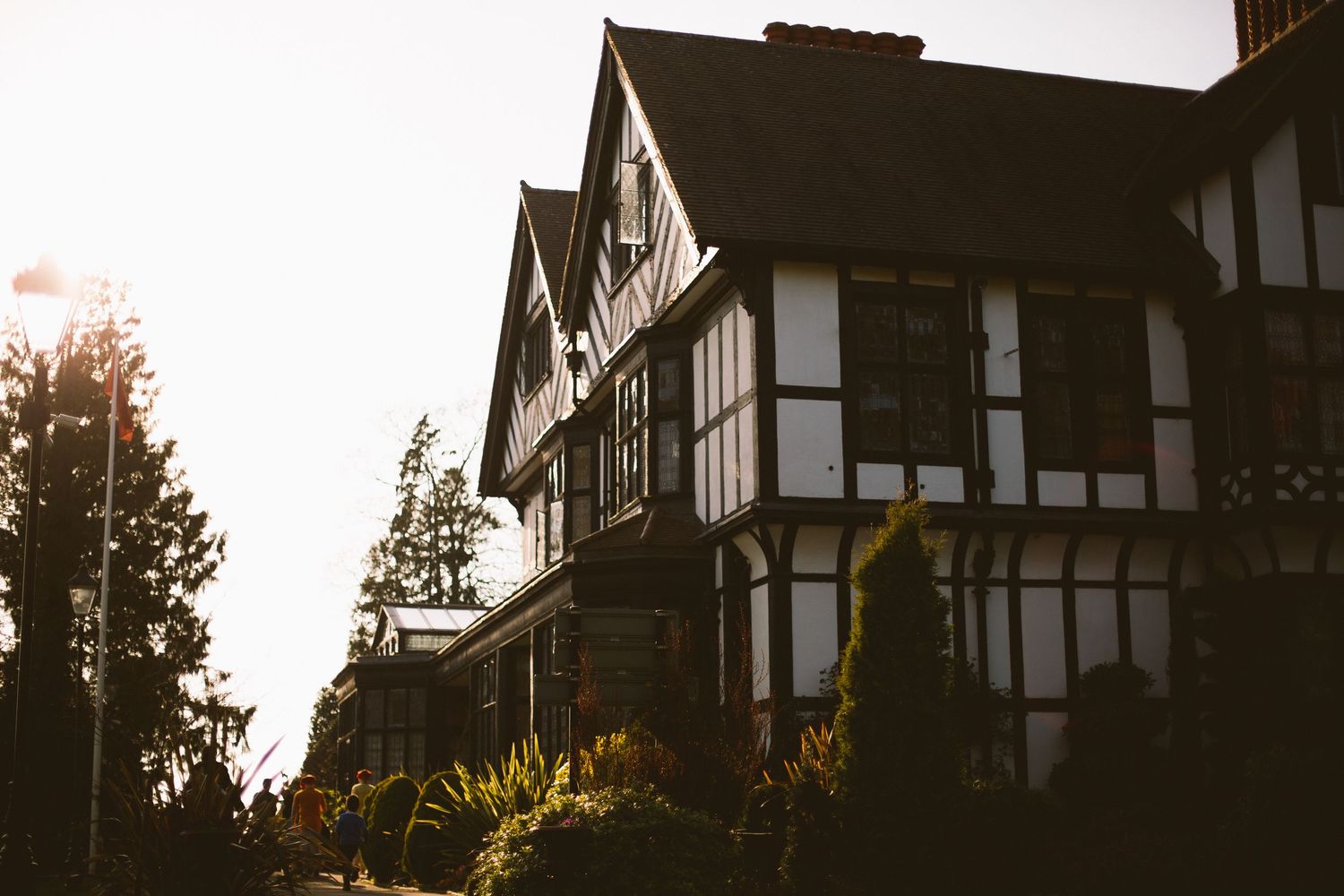 Tudor-style homes with white and dark timber framing stand against a sunset sky with trees silhouetted in the background.