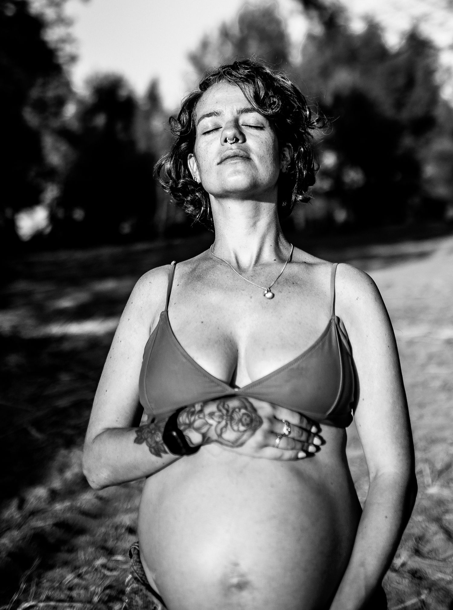 Black and white maternity portraits showing a pregnant belly in natural outdoor lighting.