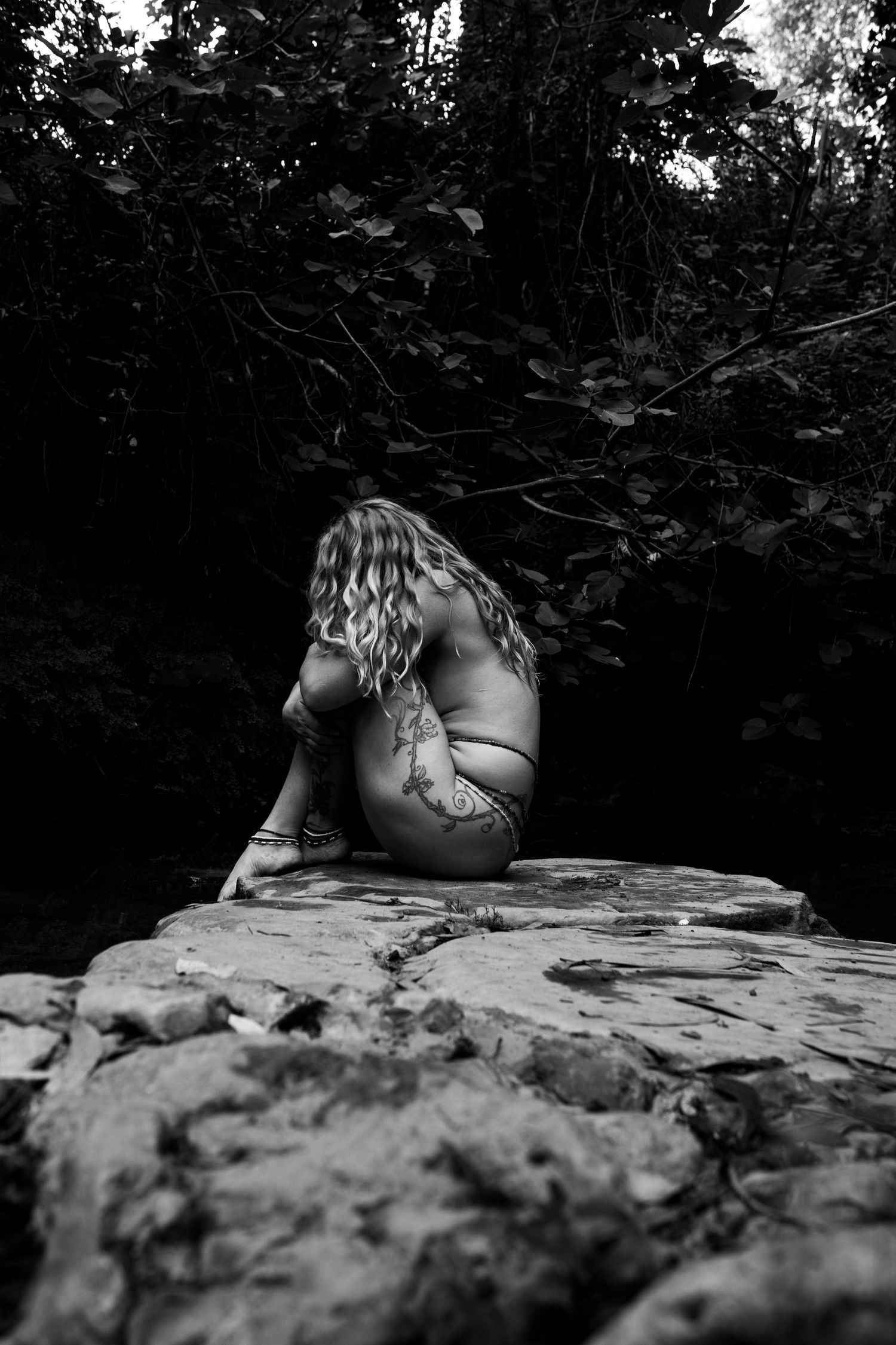 Black and white artistic portrait sequence shows a figure reclining on textured rock surface in natural setting.