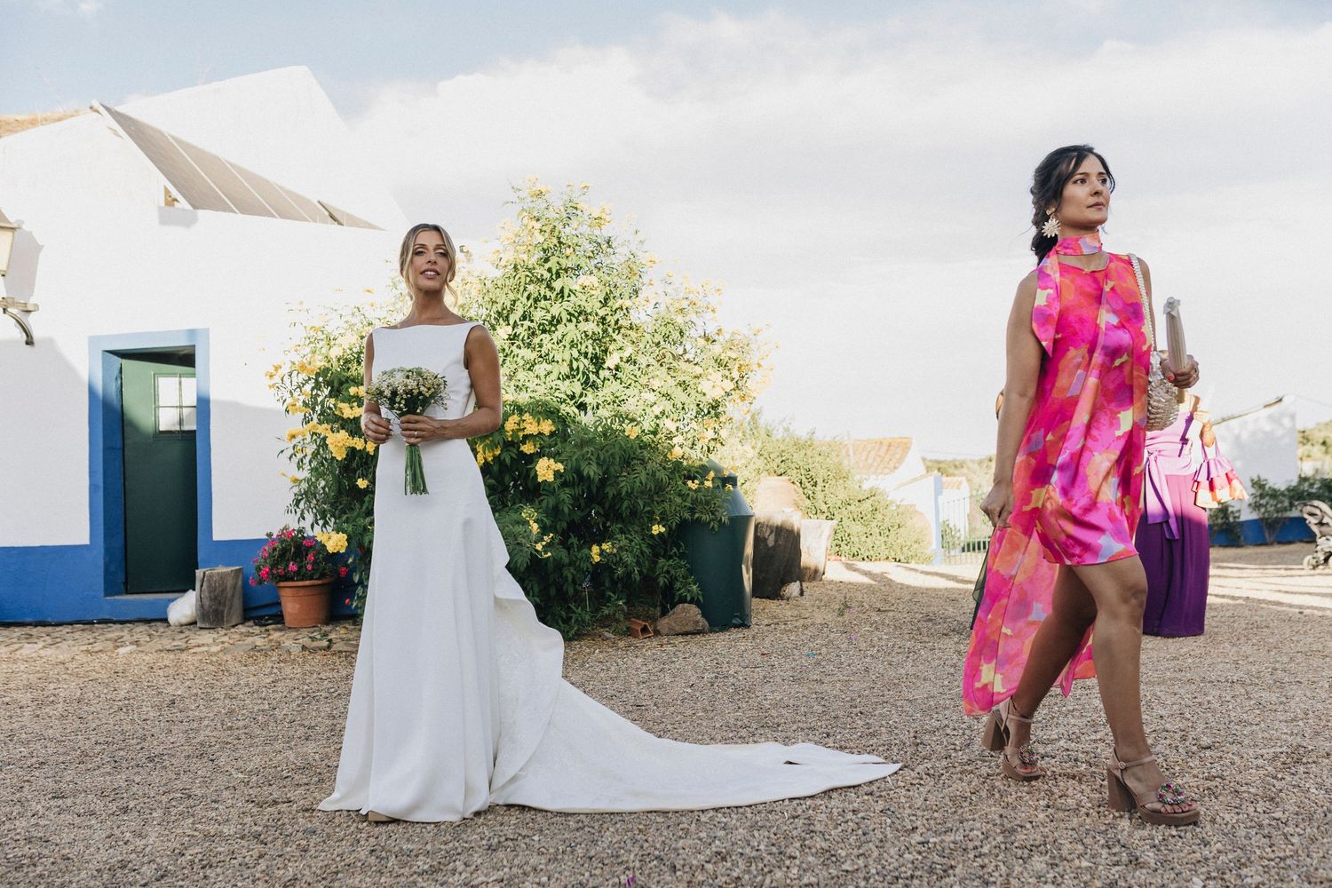 Wedding party members in colorful attire pose outside a white and blue building.