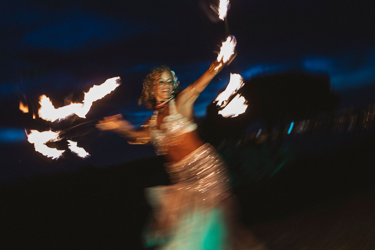 Multiple fire dancers spin flaming batons against a dark night sky creating streaks of glowing light.