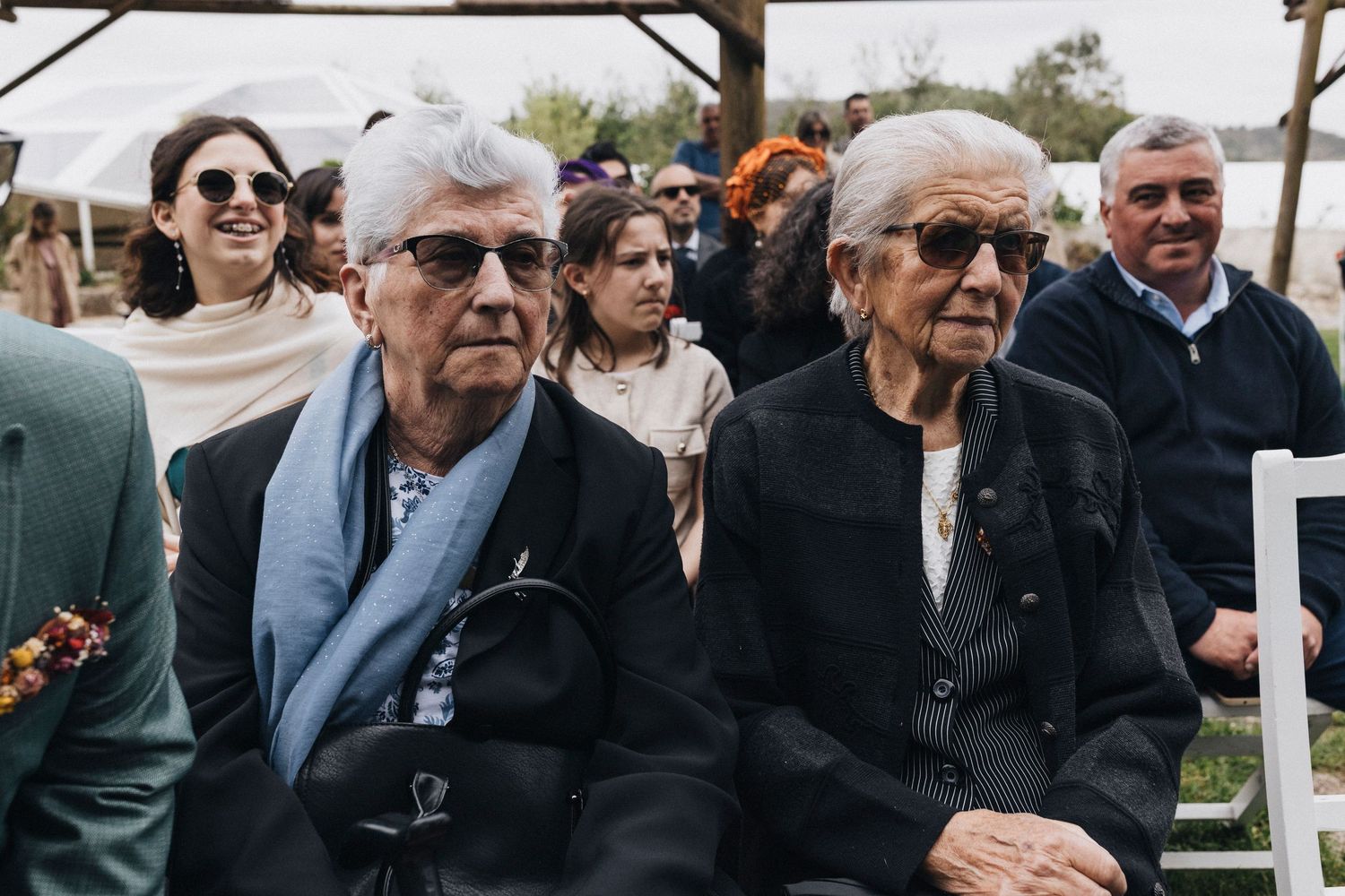 Wedding guests seated in formal attire watching ceremony outdoors.