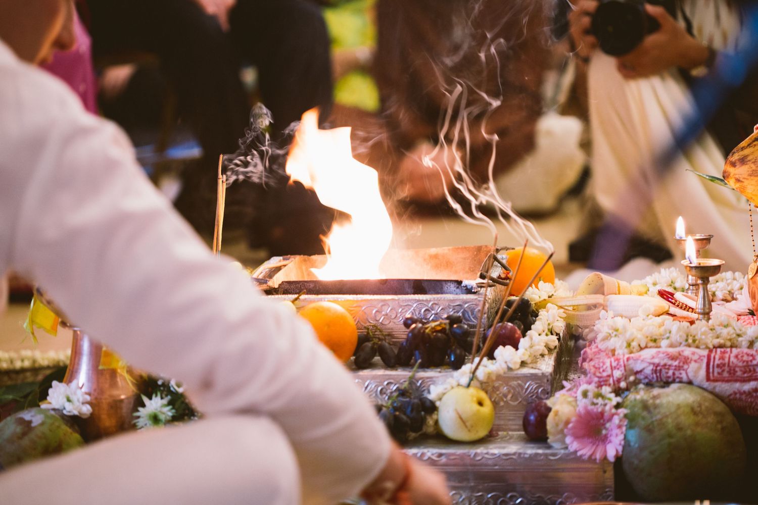 Incense sticks and flames burn during a spiritual ceremony with colorful flowers and decorative items.