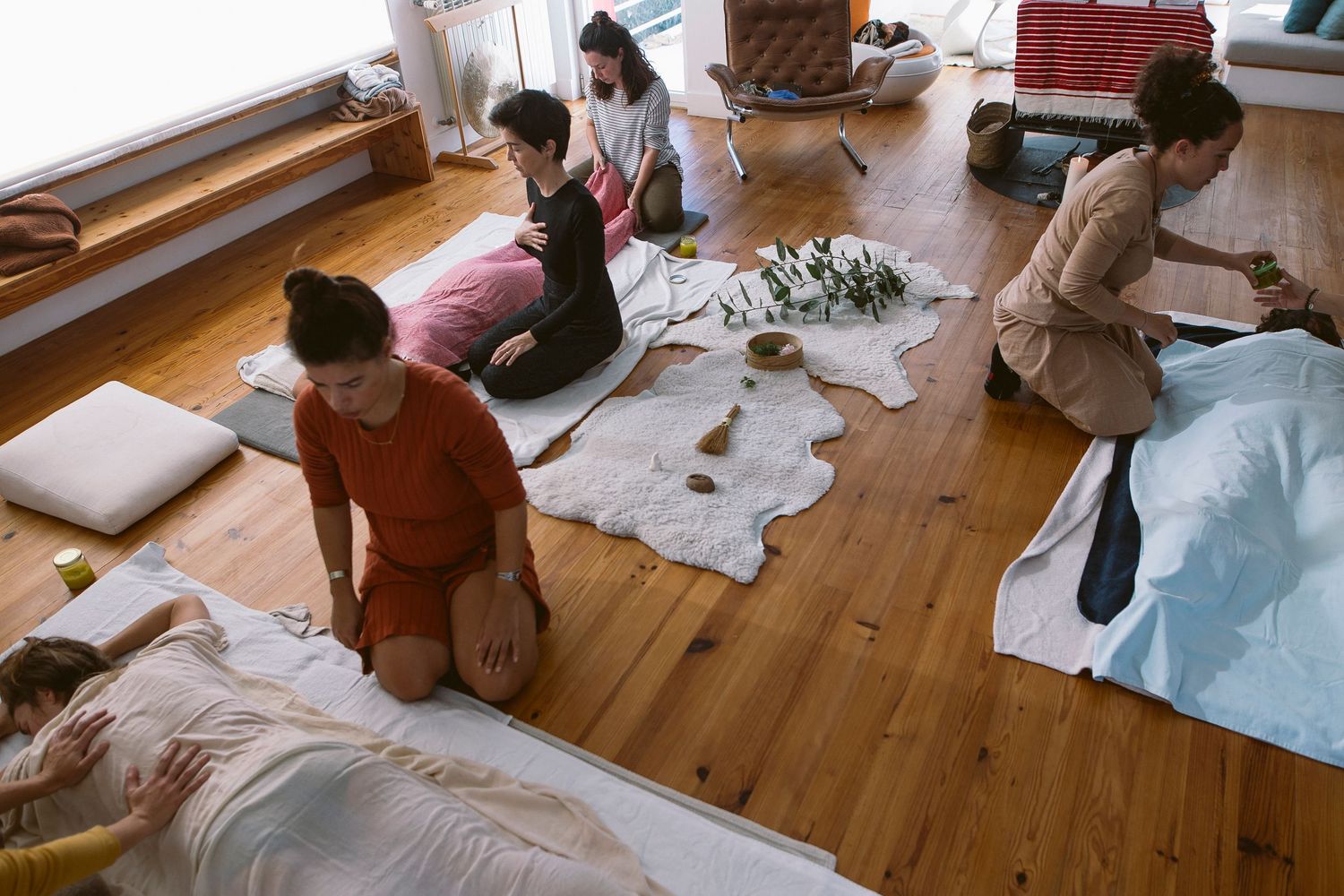 People gathered on wooden floor with white fabric and cushions during indoor activity.