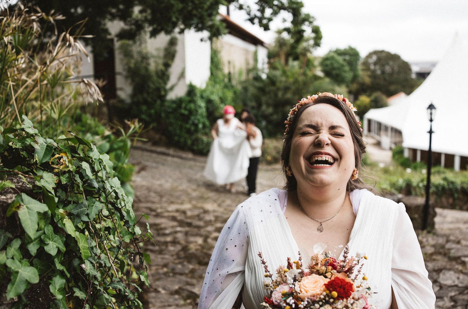 Joyful candid moment of person in white dress holding bouquet on cobblestone path.