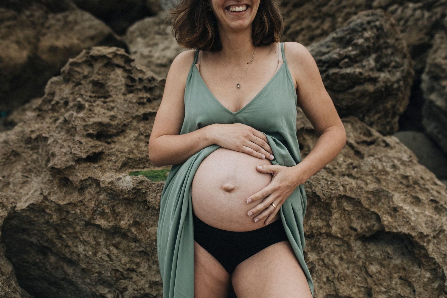 Artistic maternity photos on rocky terrain showing a pregnant woman in a mint green dress.