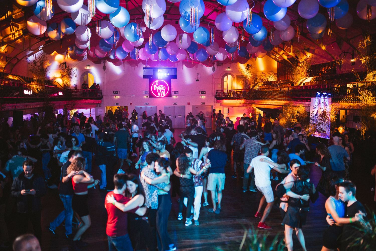 Couples dancing salsa in a vibrant nightclub with colorful purple and red lighting creating a festive atmosphere.