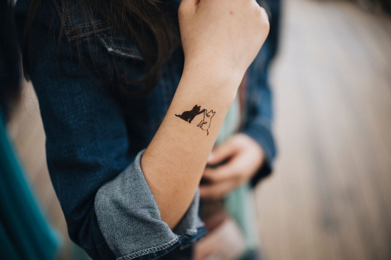 A small minimalist bird tattoo design shown on someone's forearm.