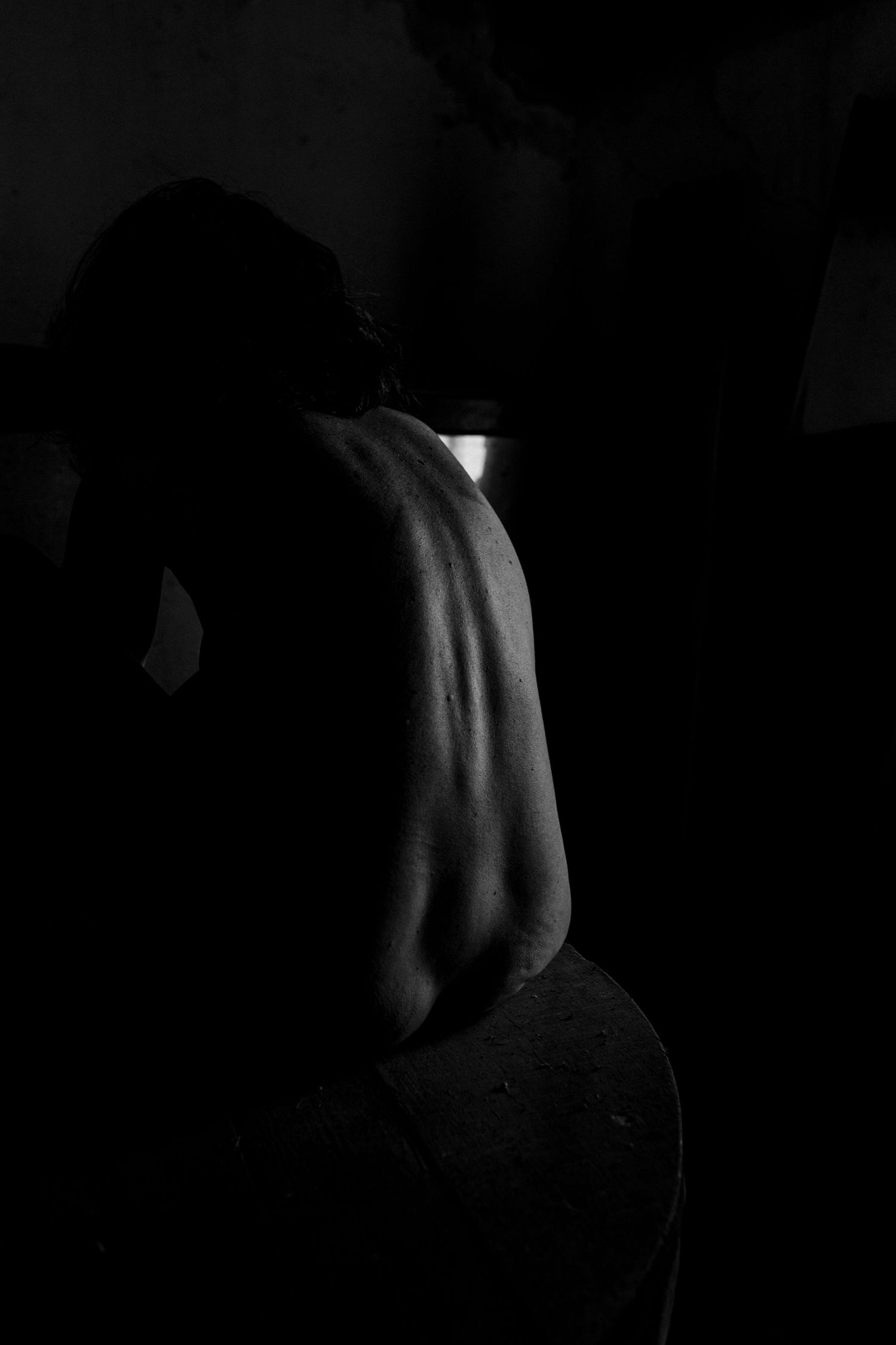 Black and white artistic photo of a person's bare back in dramatic low-key lighting against a dark background.