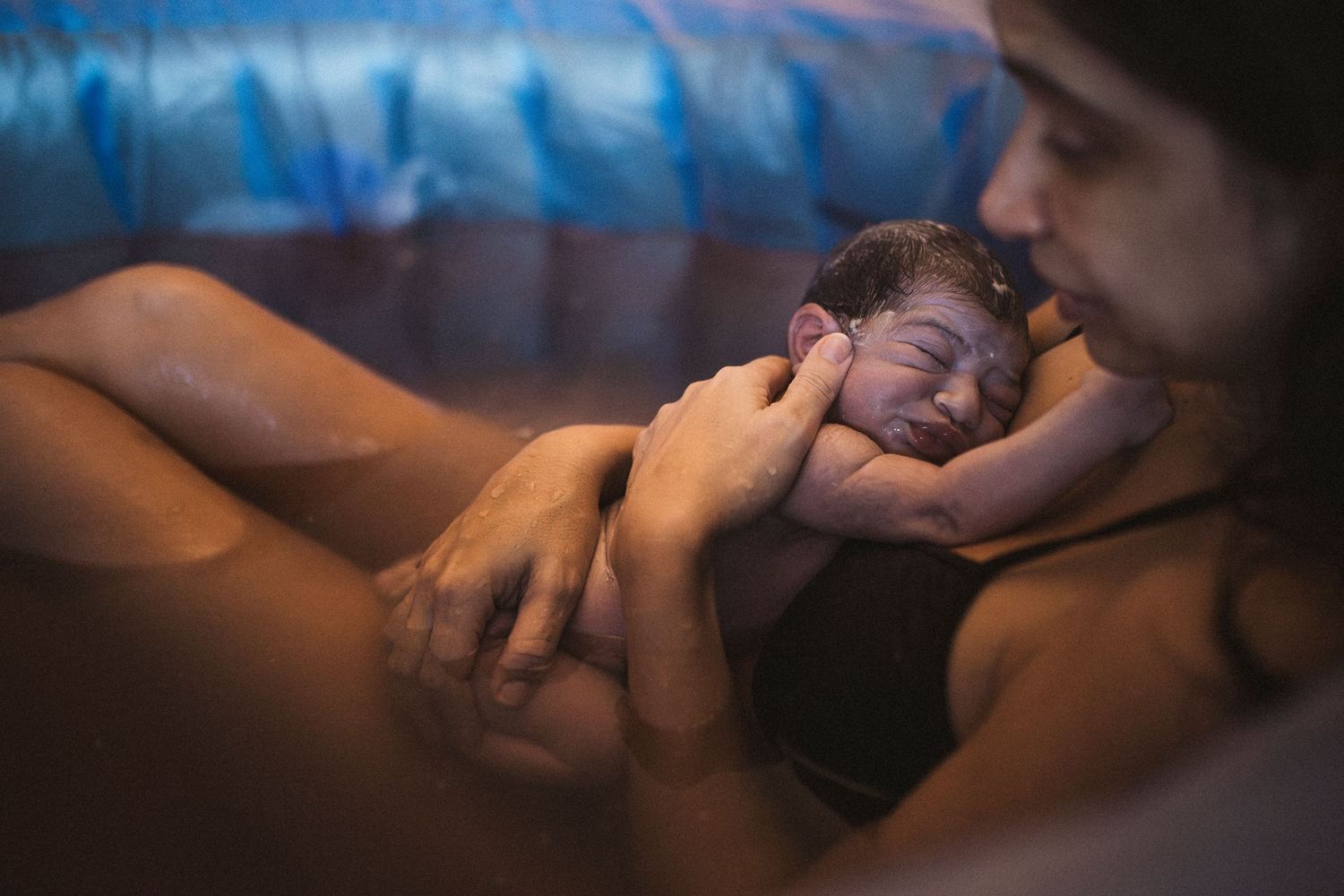 Intimate photography with blue tones capturing tender moments during a birth.