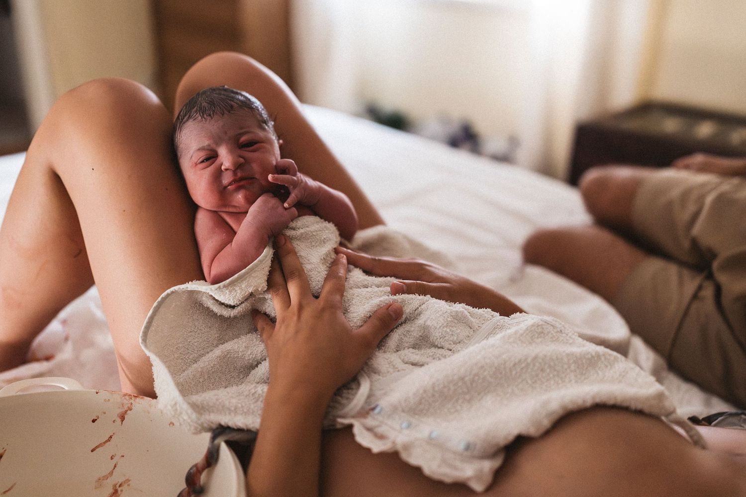 A newborn baby wrapped in a white blanket lies on a bed during an intimate moment.