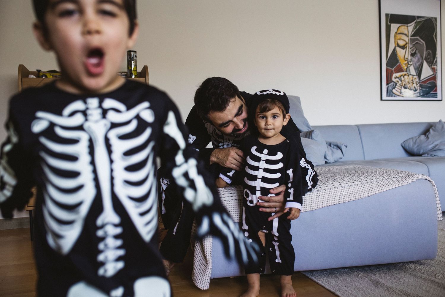 Children wearing skeleton costumes pose together during Halloween festivities in a living room.