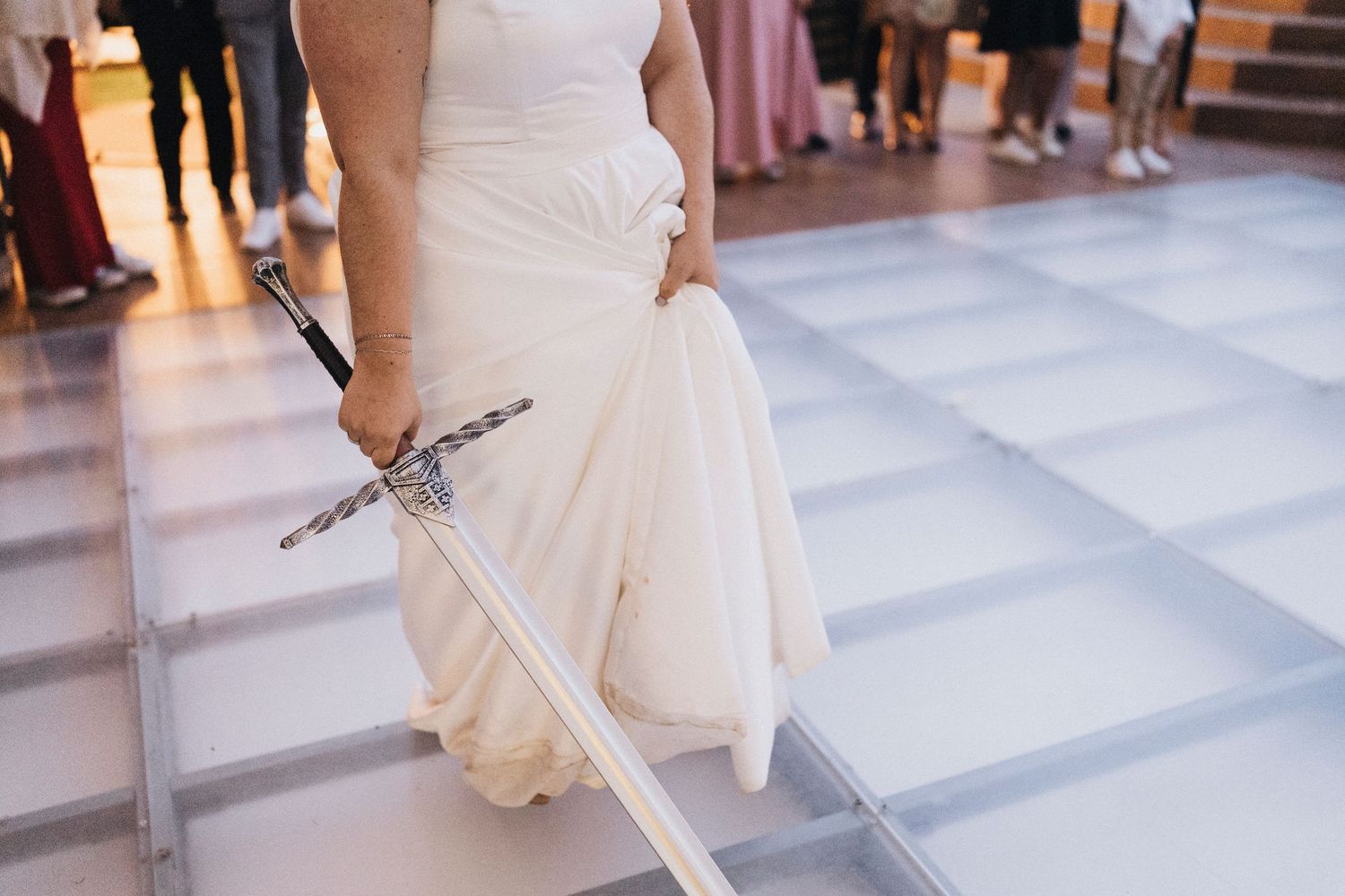 A bride in a white dress walks across a tiled floor in an indoor venue during a wedding celebration.