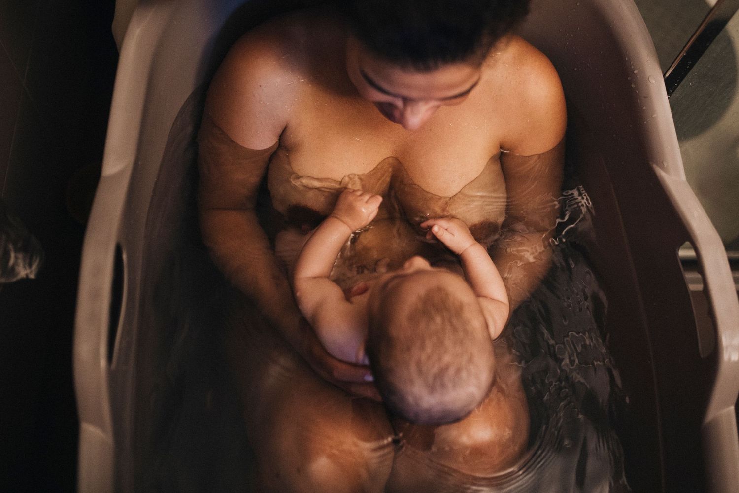 Natural breastfeeding session photographed in dark intimate setting with soft focus.