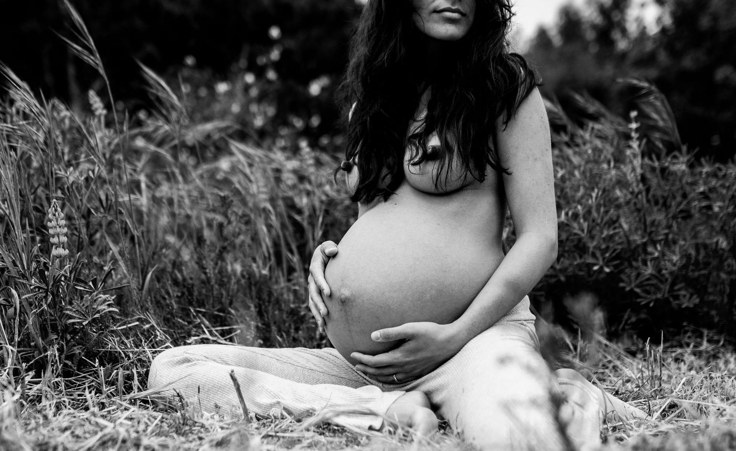 Black and white maternity photoshoot in a natural outdoor setting with tall grass.