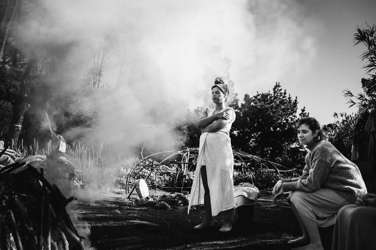A black and white photo of people gathered outdoors with smoke or steam rising in the background during a social gathering.