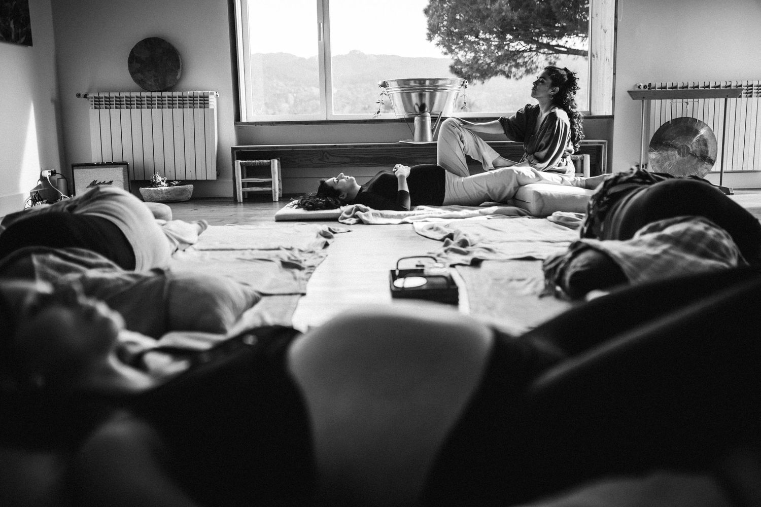 A black and white photograph shows a messy bedroom with someone sitting on a bed playing guitar.