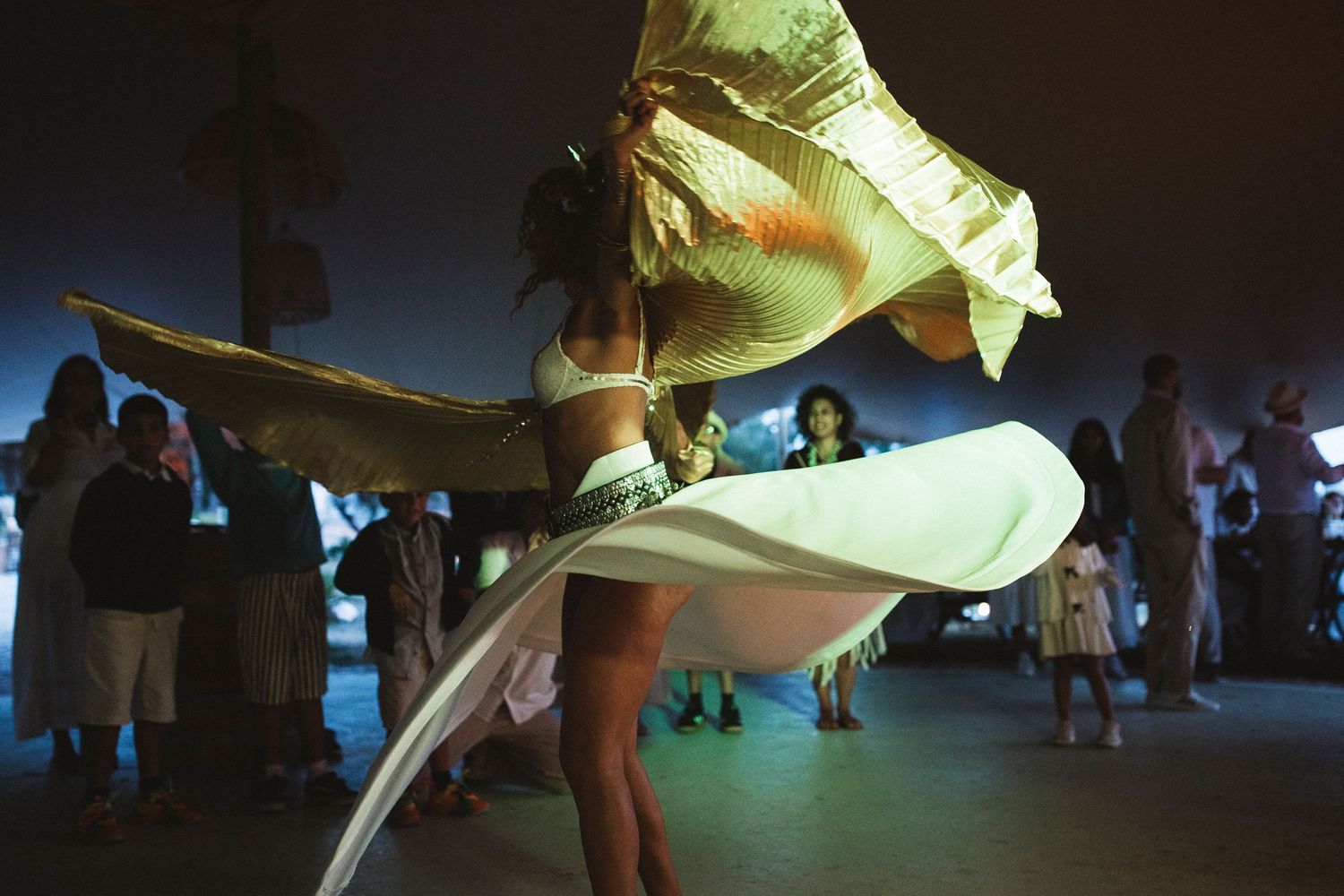 A dancer in a flowing yellow dress twirls during a performance, creating dramatic movement in dim lighting.