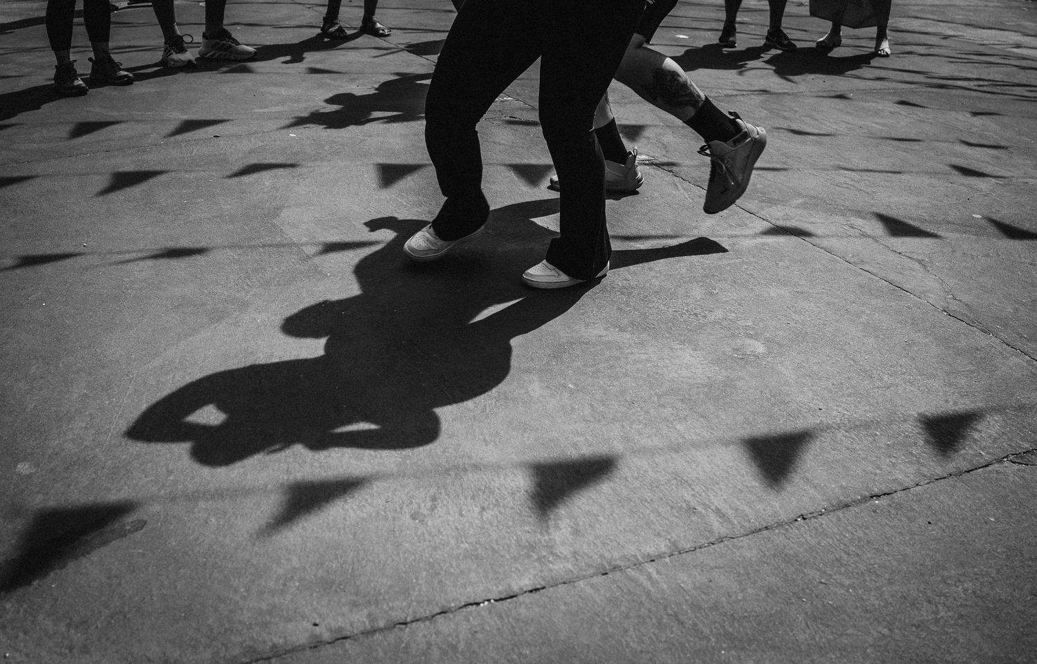 A black and white photo of shadows cast by people walking on a sidewalk during daytime.