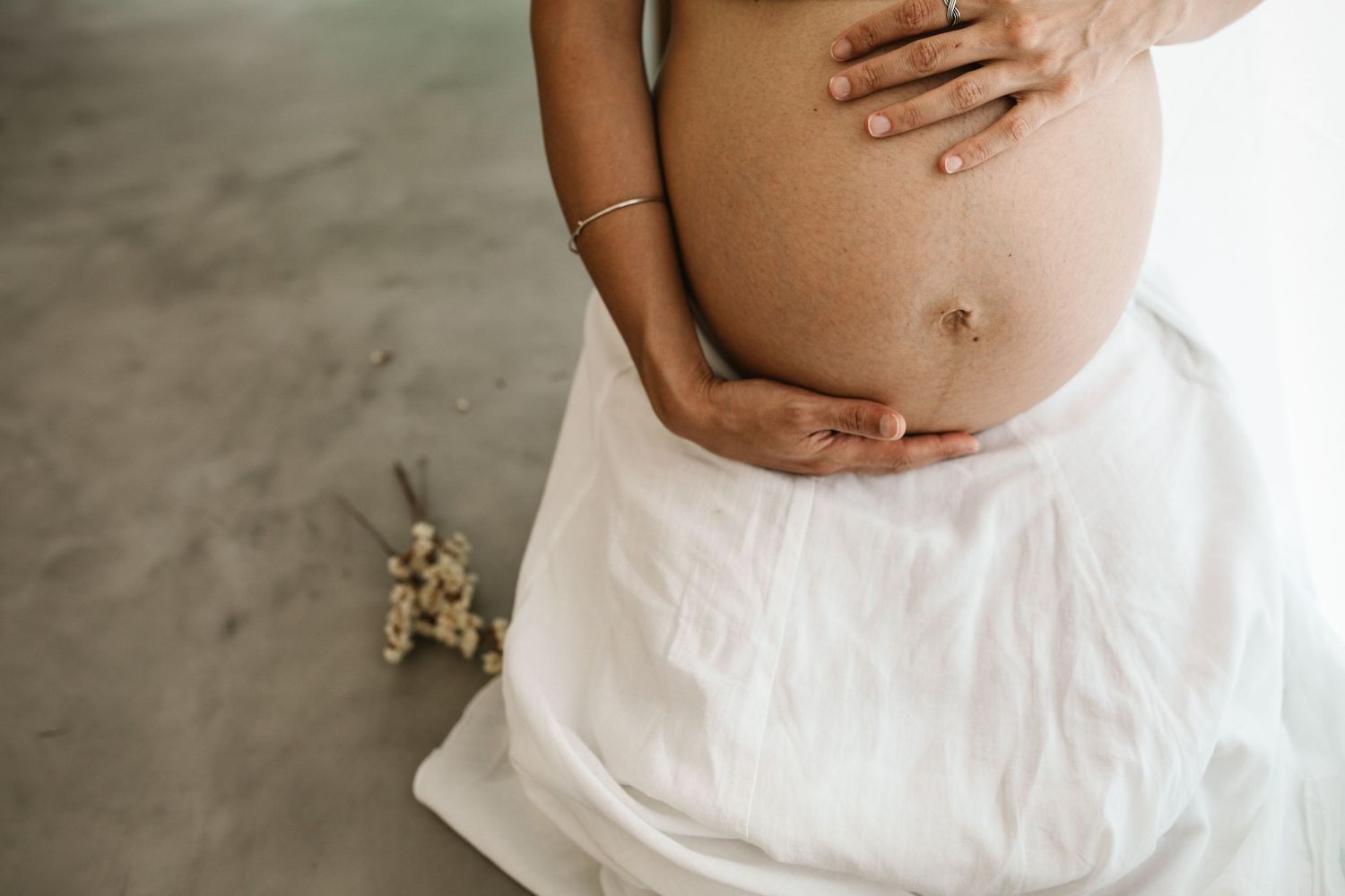Series of maternity photos showing pregnant belly in white dress against neutral background.
