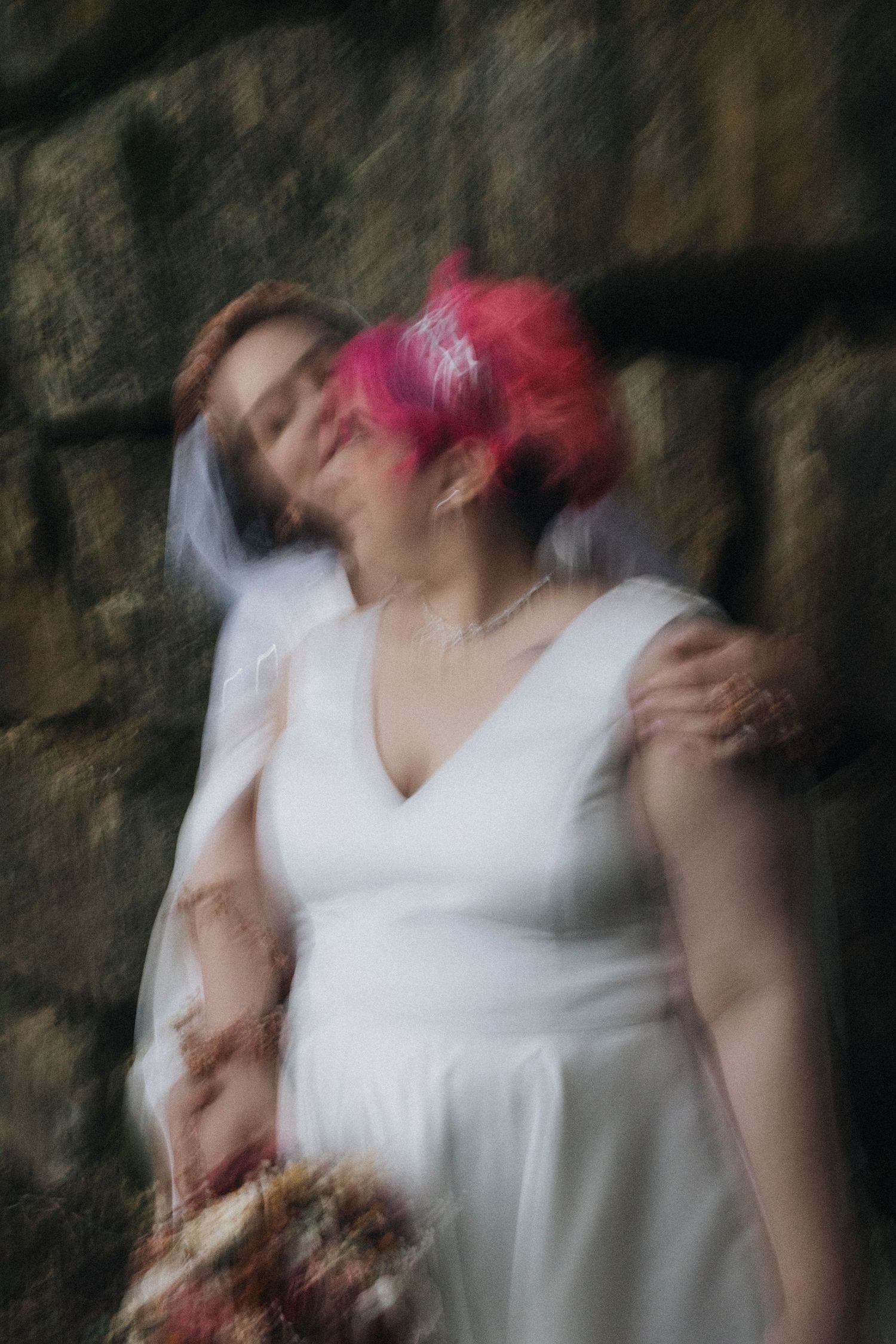 Artistic motion blur captures dancing in white wedding dress against stone wall.