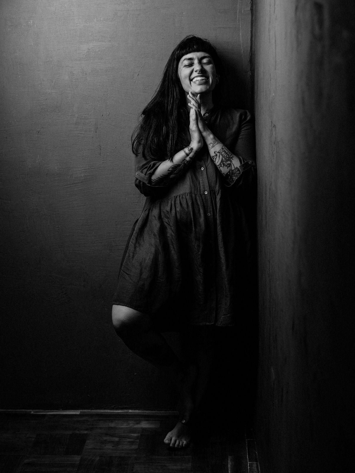 Person in flowing dress leans against wall in moody black and white photograph.