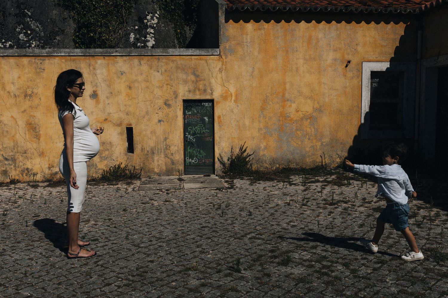 People walk along a cobblestone street next to weathered yellow walls in an old historic district.