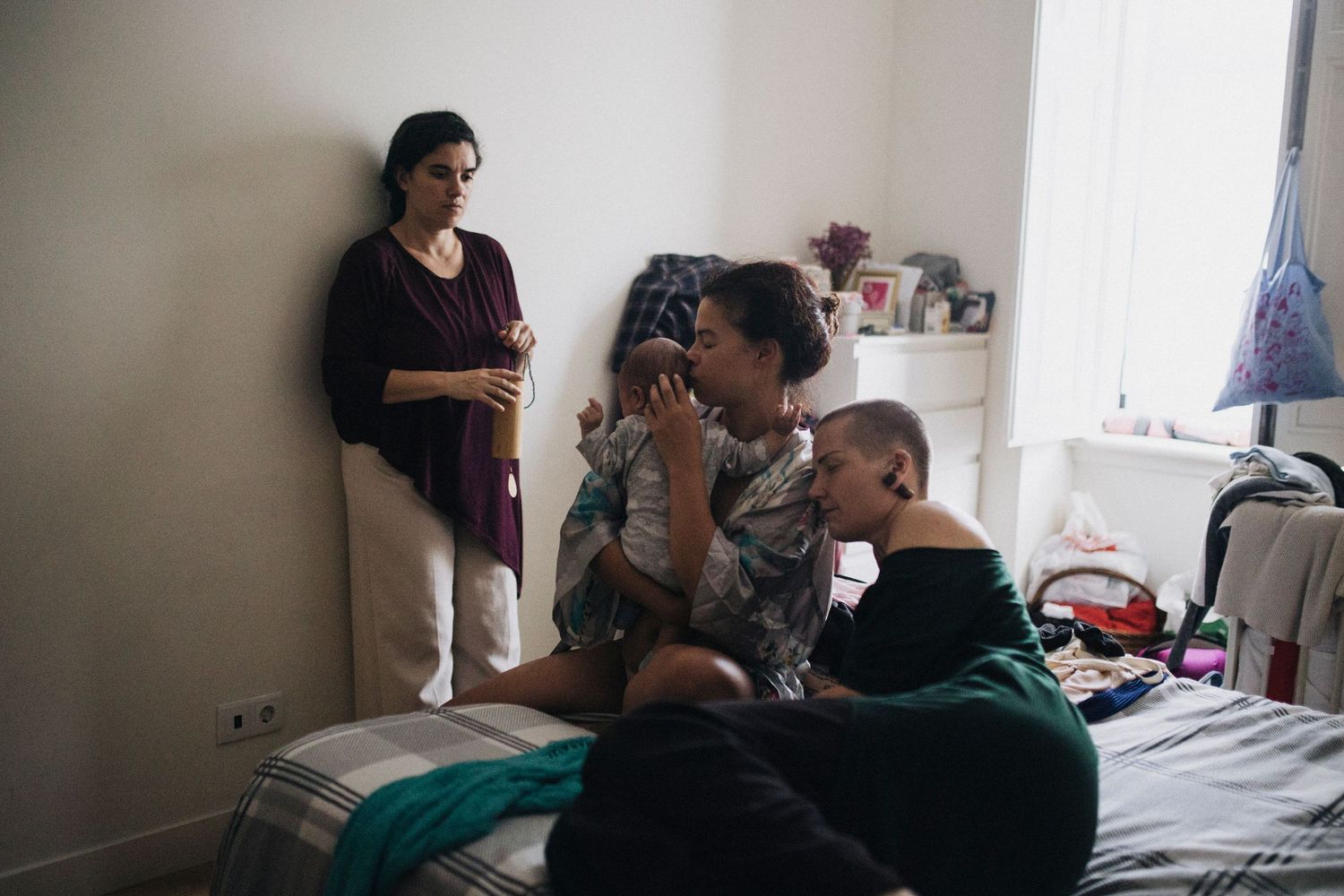 Family members gathered around during intimate feeding time in bedroom setting.